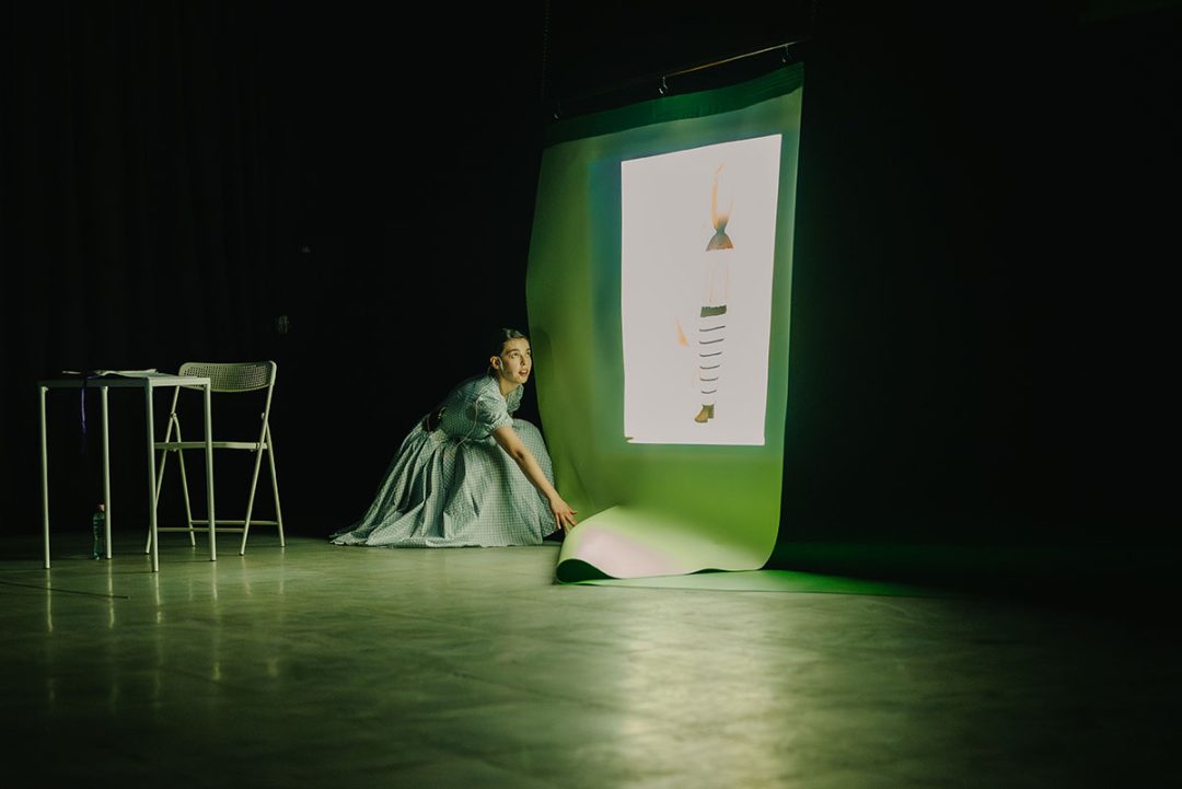 Woman kneeling beside illuminated screen in dark studio
