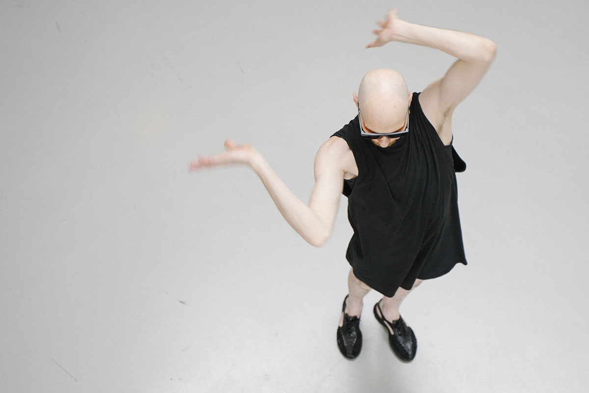 Bald person in black outfit posing expressively