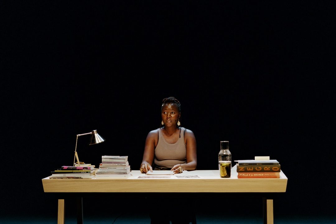 Woman seated at desk with books and lamp