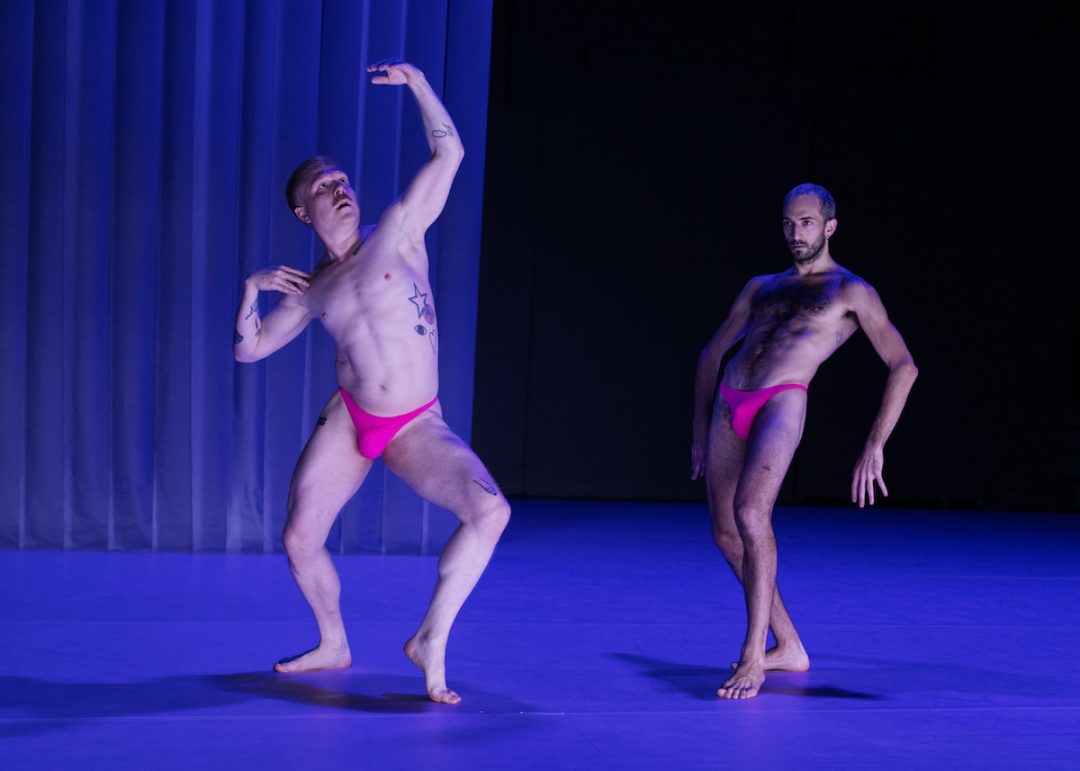 Two male dancers in pink briefs performing on stage