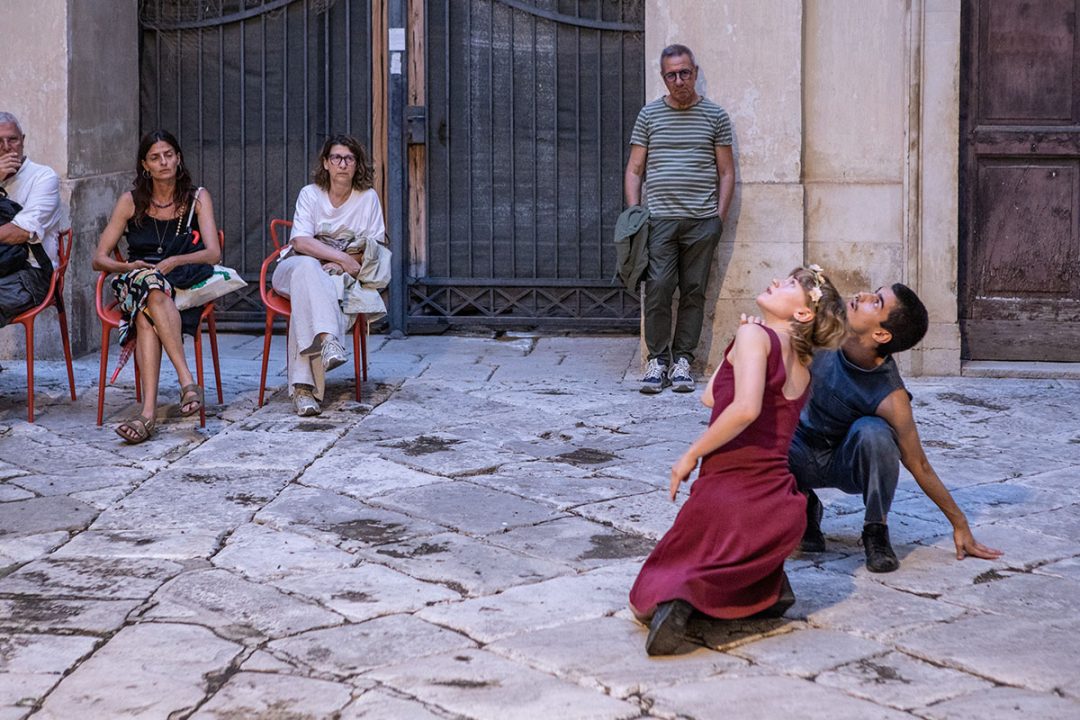 Two dancers performing in stone courtyard before spectators