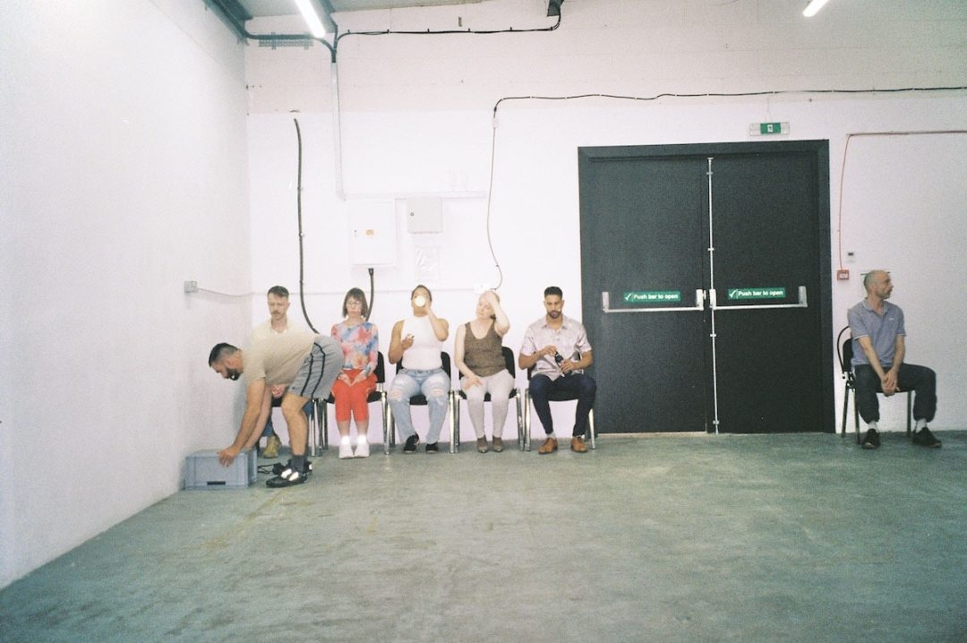 People seated in sparse room beside exit doors