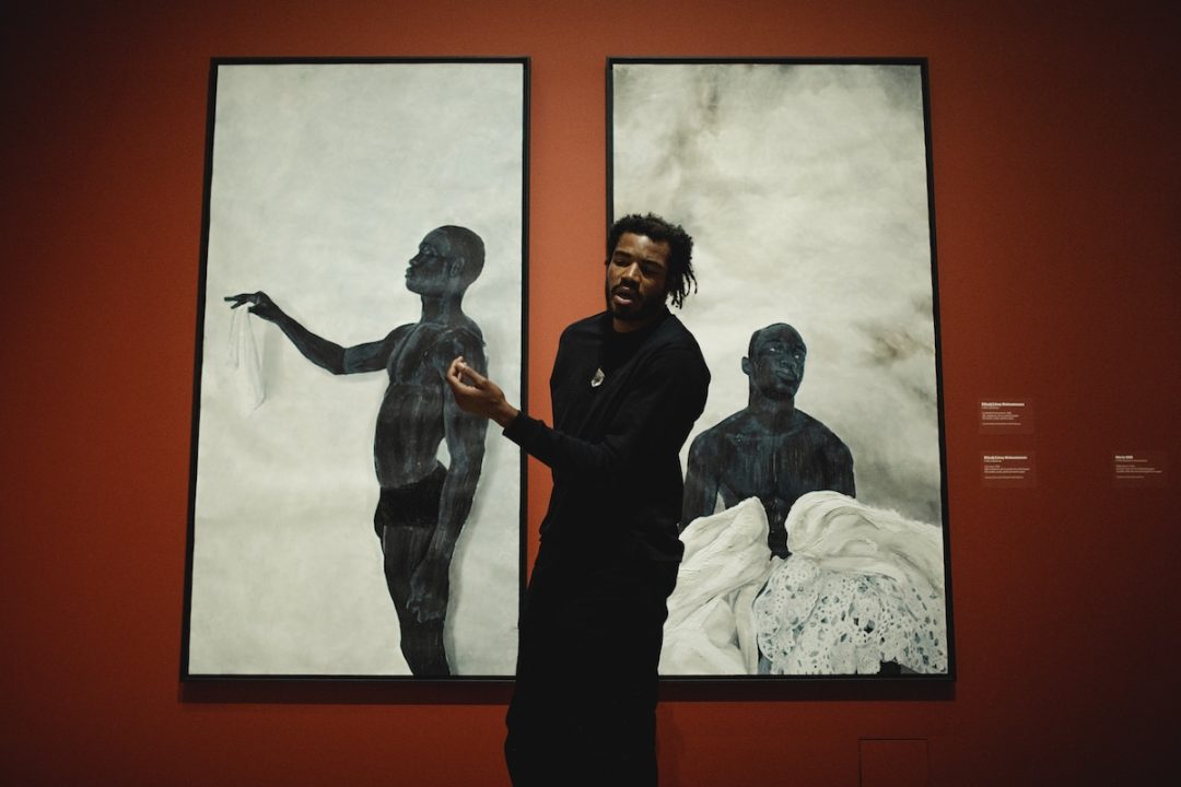 Man standing before large paintings in gallery