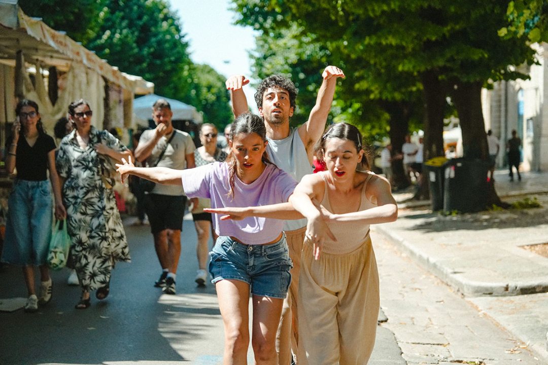 Three dancers performing in sunny street with onlookers