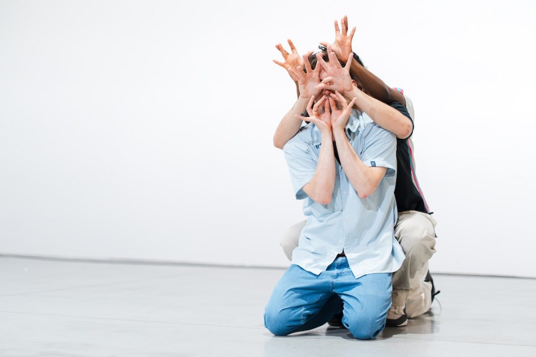 Person kneeling with two people hidden behind – multiple hands cover the front face