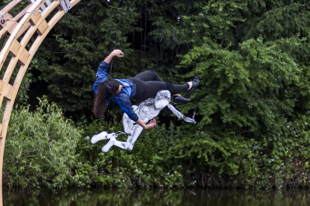 Woman suspended with puppet over lake woodland setting