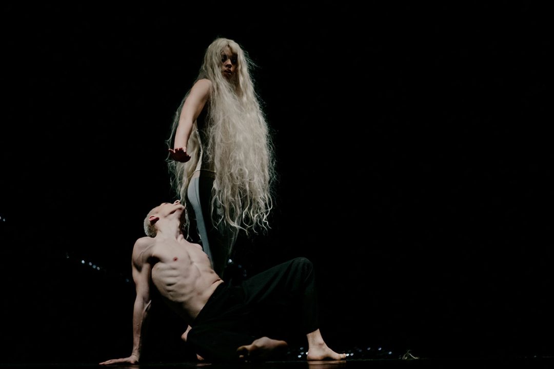 Contemporary dancers performing dramatic duet on dark stage
