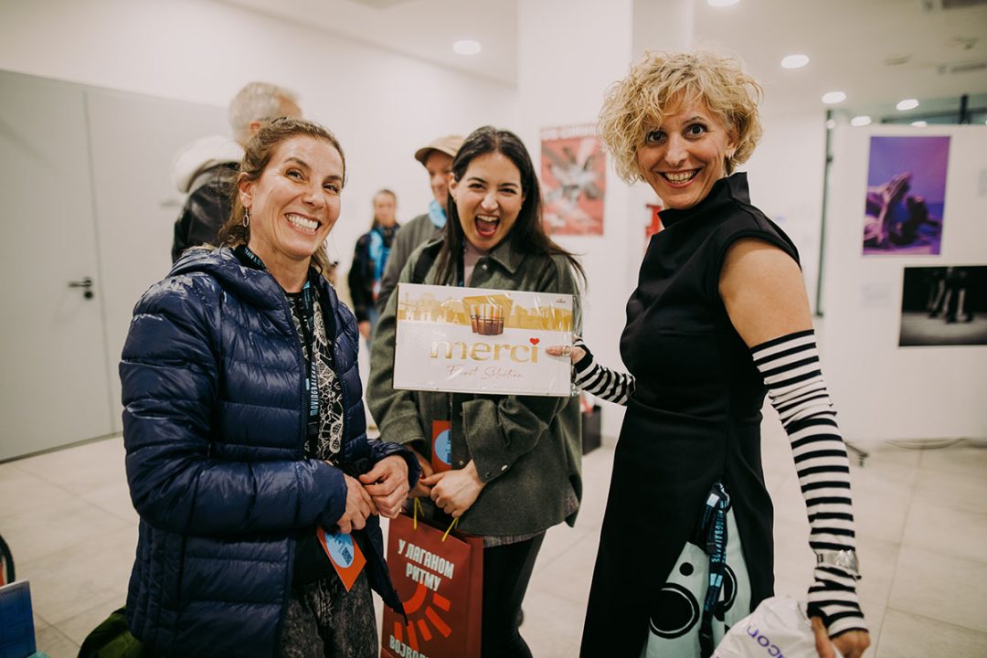 Three women smiling, holding box of Merci chocolates