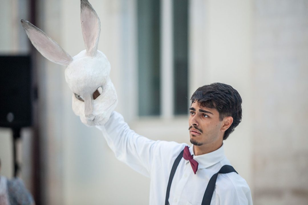 Man holding white rabbit mask aloft outdoors
