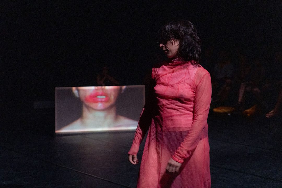 Performer in red dress with projected lips backdrop