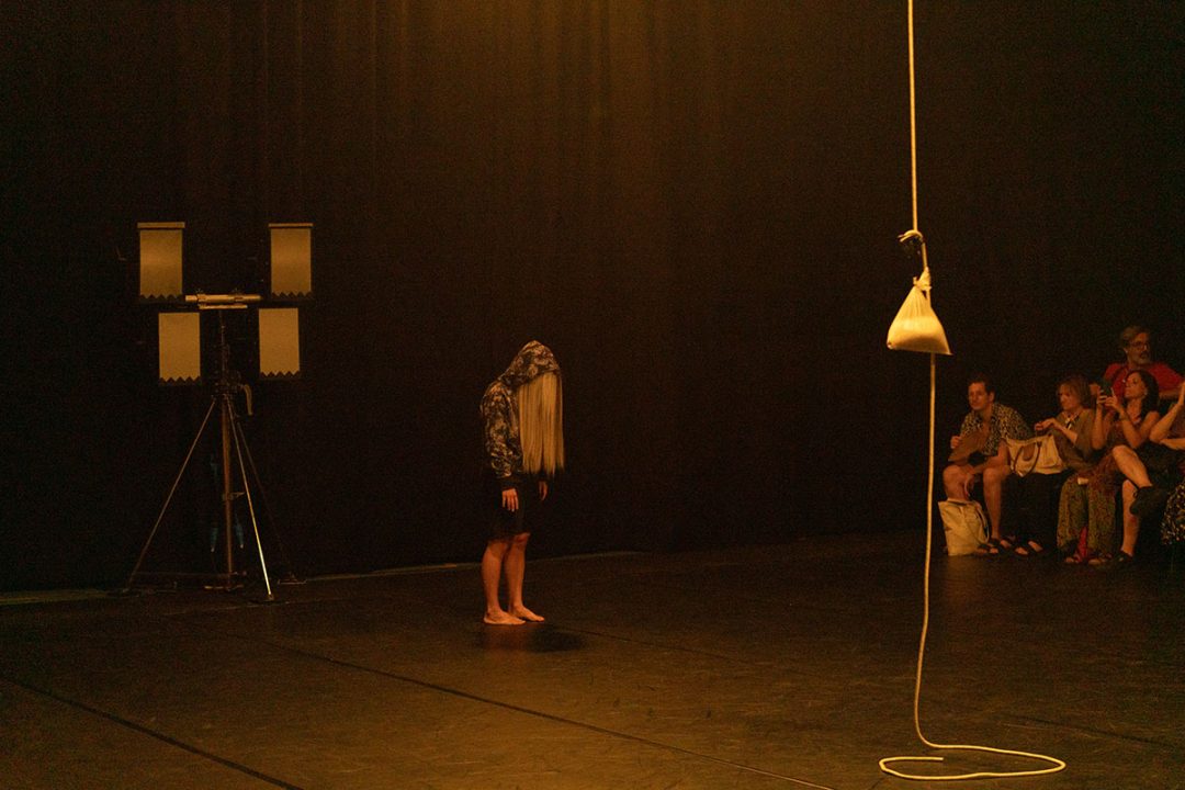 Barefoot performer under warm light before seated audience