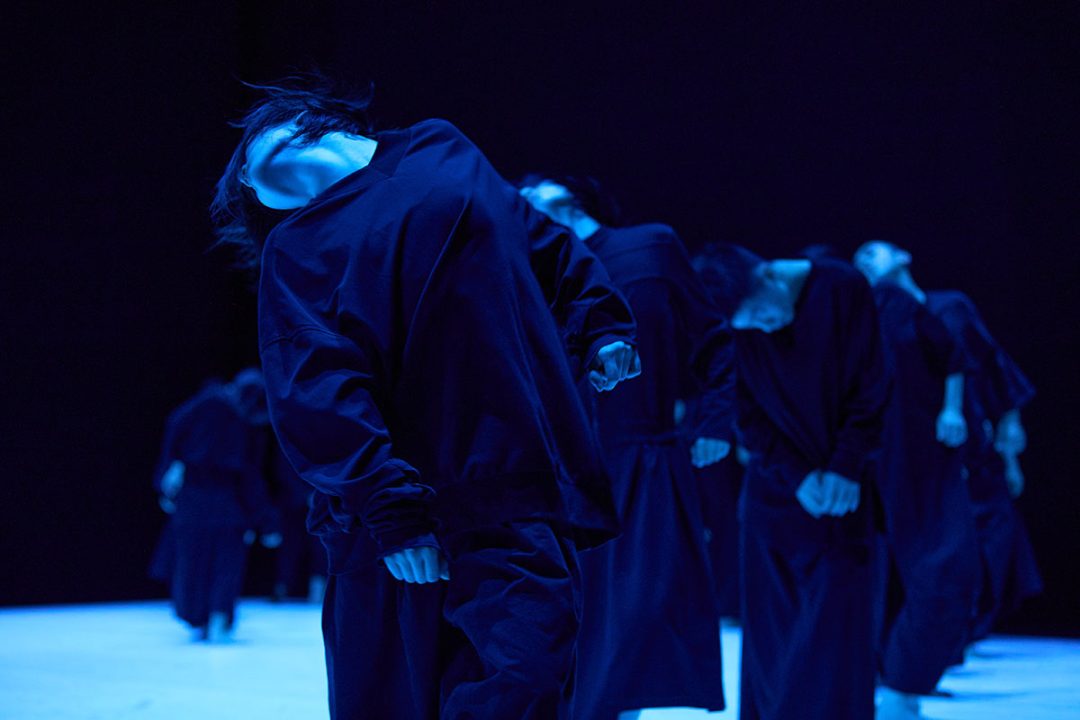 Dancers in dark clothing performing under dramatic blue lighting