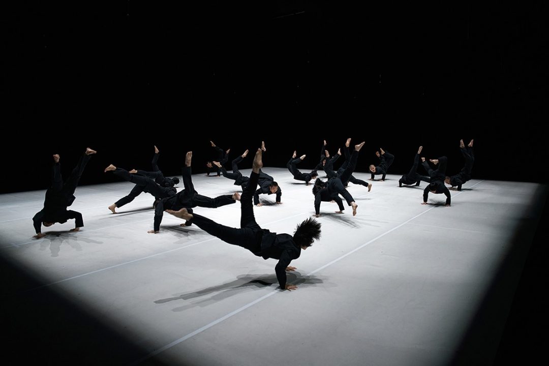 Contemporary dancers performing acrobatic floor movements on a dark stage