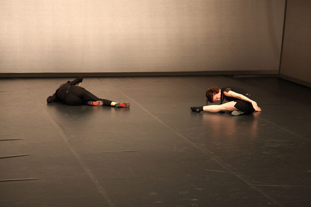 Two dancers lying on a dark theatre stage