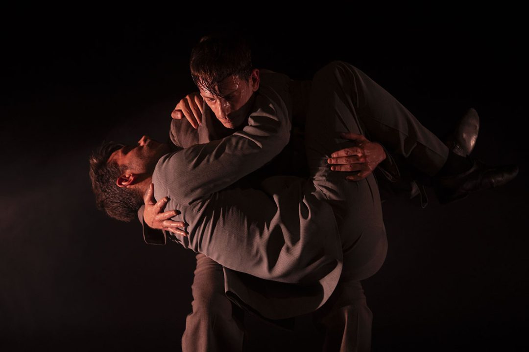 Two men in suits embracing during a dramatic stage performance