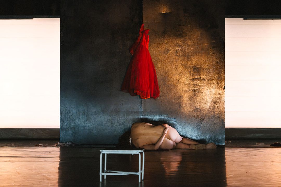 Nude person curled beneath a hanging red dress