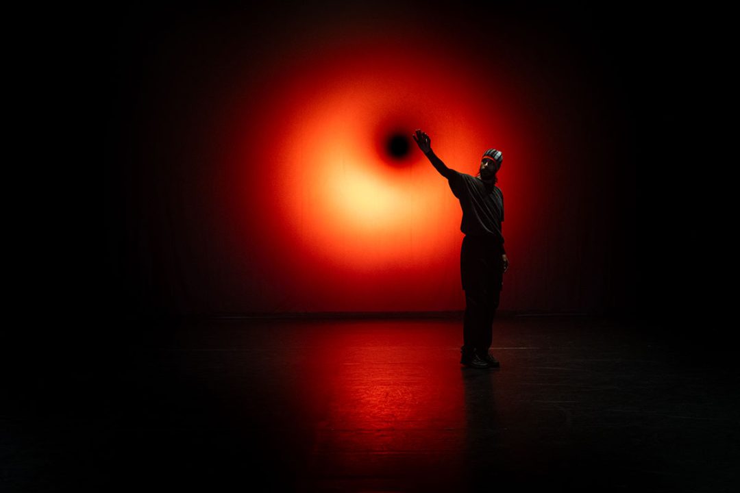 Dancer raises arm before glowing red stage light