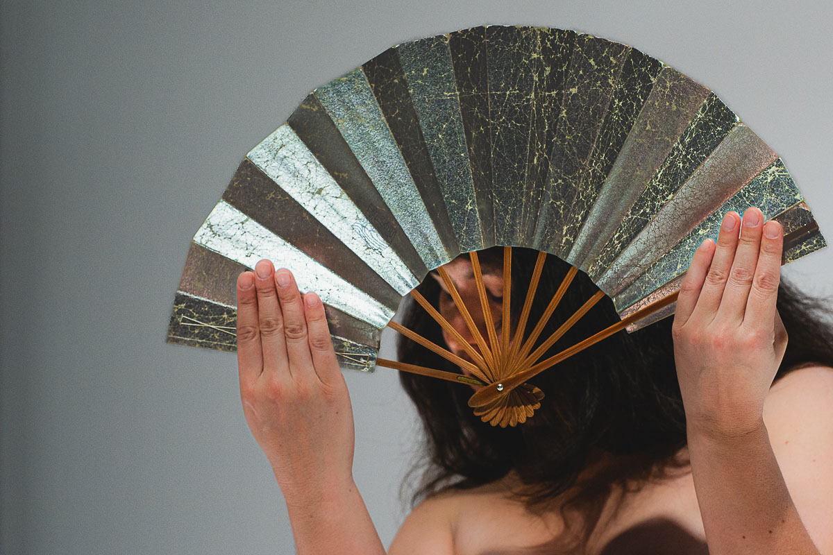 Person holding a decorative folding fan above their head