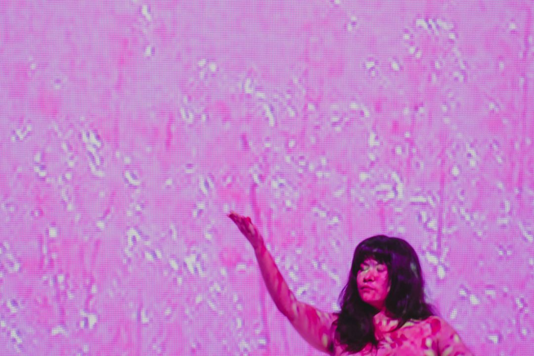 Performer with raised arm against vivid pink textured backdrop
