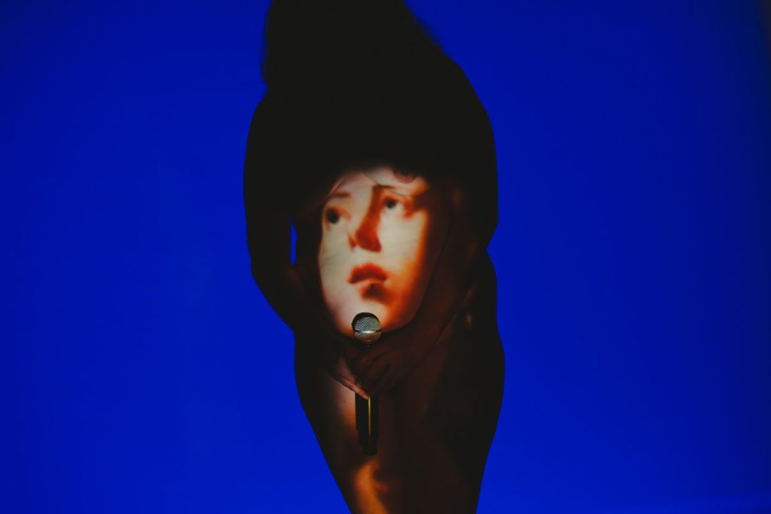 Shadowed performer holding microphone against vivid blue background